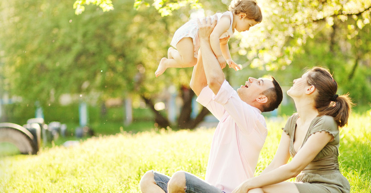 Smiling woman with young man playfully lifting baby in the air 