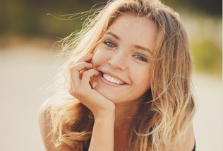 Smiling young woman with hand on chin, sitting outside