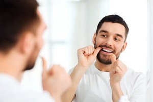 man flossing in bathroom mirror