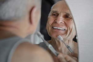 Man smiling while brushing his teeth in mirror