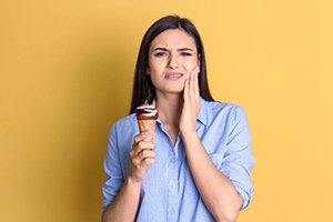 A woman holding her cheek in pain with an ice cream cone in the other hand