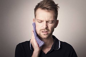 A man holding a cold towel up to his cheek 