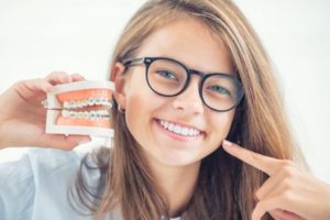 Teen holding a dental demonstration model with braces while pointing to her white teeth and smiling