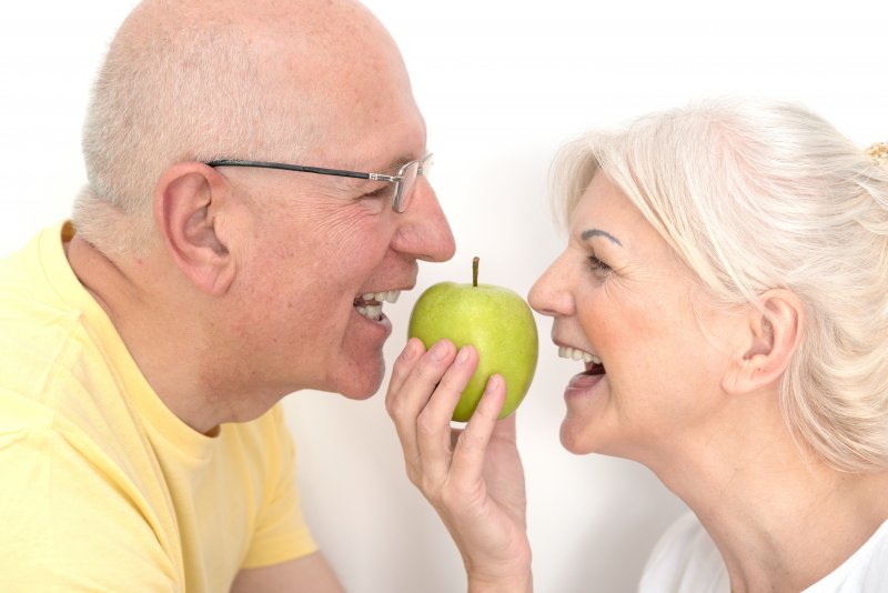 An older couple with dentures about to bite an apple